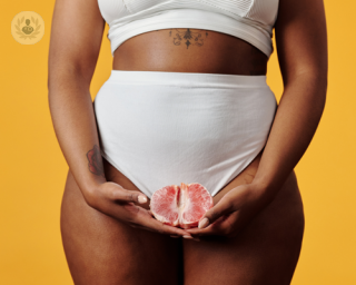 A pciture of a woman posing with a grapefruit covering her genitals 