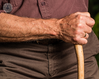 An old man's arm holding a walking stick.