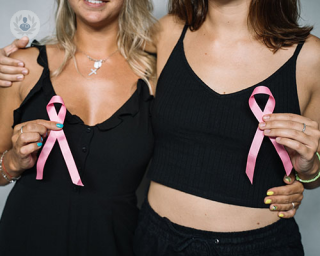 Two women wearing black clothes hold up a pink breast cancer awareness ribbon.