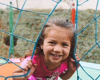 Little girl smiling next to a climbing frame in a playground