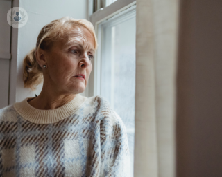 Older woman with a concerned expression looking out of a window