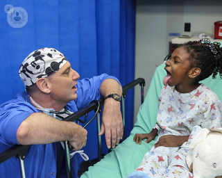 A young child on a hospital bed showing the back of her throat to a paediatric ENT surgeon.