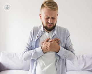 Young man stood by a sofa, holding his chest because of heartburn