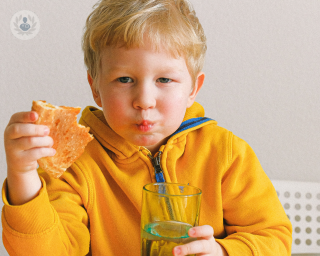 Child wearing a yellow jacket eating a pizza and holding a glass of water