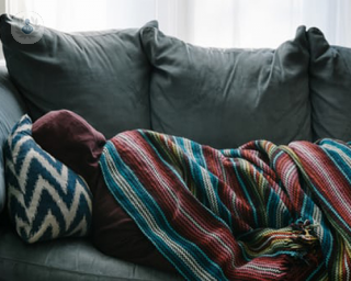 A person not feeling well is wrapped in a blanket and laying on the sofa.