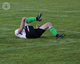 A footballer lying on the pitch clutching his right knee in pain.