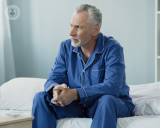 A man sitting anxiously at the end of a hospital bed. 