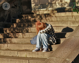 A young redhead girl sat on a staircase hiding her face between her legs