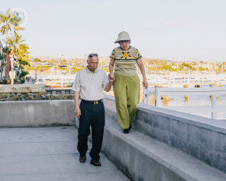 Elderly woman walking on a wall and being supported by elderly man