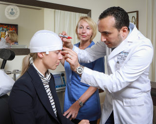 Woman having her head measured and wearing a white cap, preparing herself for a TMS session.