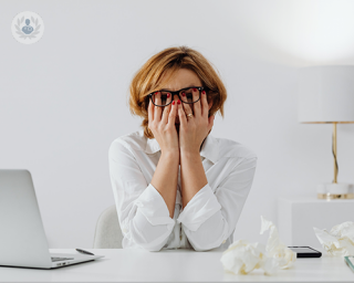 An adult woman in front of her computer, feeling overwhelmed and stressed.