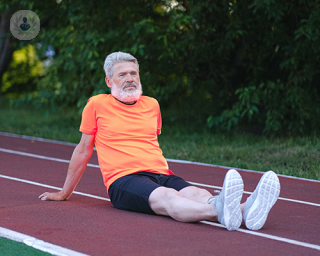 An elderly man resting on a running track wearing sports clothes
