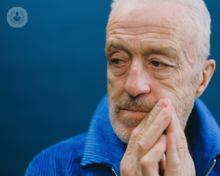 Concerned older man with his hands to the side of his mouth, wearing a blue jacket against a blue background