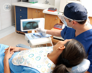 A female patient is laying on a reclined dentist chair and her dentist is sitting next to her. Both are looking at an x-ray of the patient's mouth while the dentist explains the treatment to relieve the patient's dental phobia.