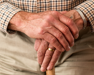 A close up of an elderly man's hands on the top of his walking stick. Many patients with Parkinson's disease require a walking aid for stability.