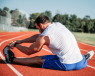 A sportsman sitting on a running track and stretching their knee