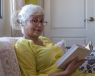 An elderly woman sat on a sofa reading a book