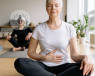 Older woman calmly sat on a yoga mat with closed eyes and her hands on her stomach  
