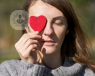 Young woman in the sunshine holding red paper heart cut out to her eye