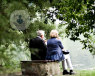 Two elderly people sat on a bench looking at a lake