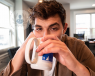 A young man looking tired while drinking a cup of coffee.