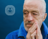 Concerned older man with his hands to the side of his mouth, wearing a blue jacket against a blue background