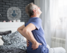 Elderly man sitting on his bed and holding his lower back in pain