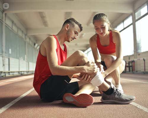 Woman helping sportsman with leg injury during cardio training