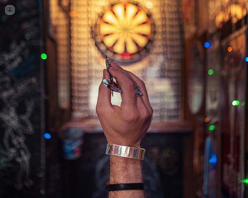 Focus on hand about to throw a dart at a darts board in a bar or pub