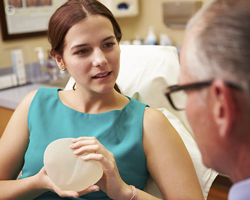 A woman holding a breast implant during a consultation with a plastic surgeon. Breast implants are the most common causes of capsular contracture, in which a capsule of fibrous skin develops around the implant to barricade it from the body.