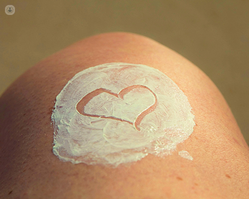 Close up of a person's knee with a sun cream on, which is useful for taking care of moles. 