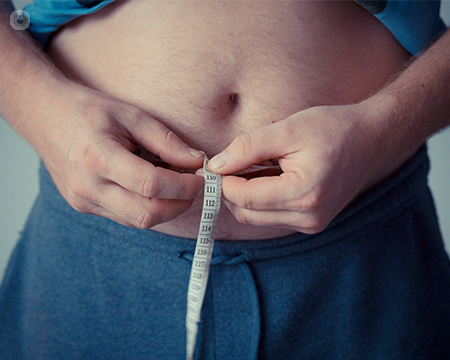 A man's overweight stomach with a tape measure around it.