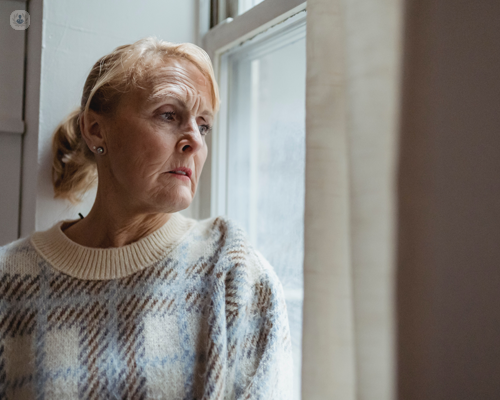 Older woman with a concerned expression looking out of a window