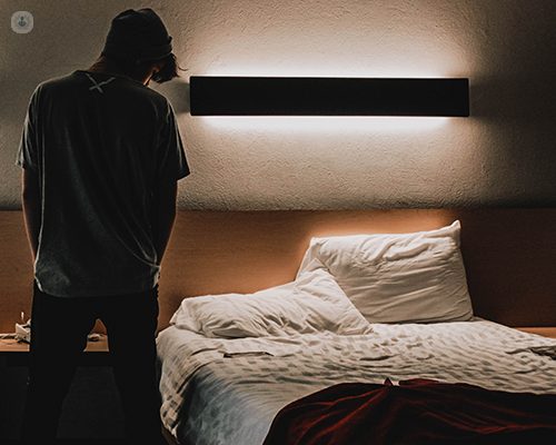 A man in a dimly lit room looking at a bed