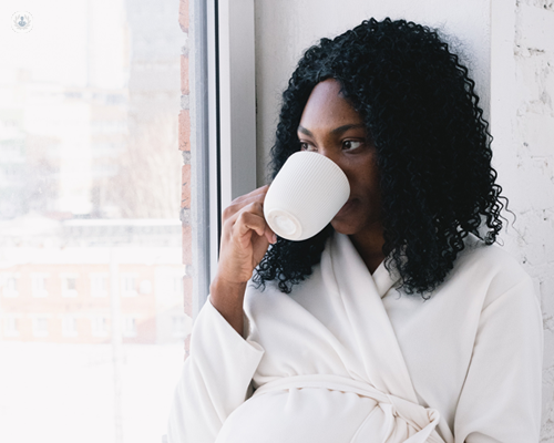 Pregnant woman with adenomyosis sat by a window while drinking from a mug