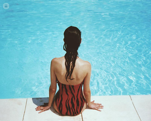Girl in swimming costume sat poolside. 