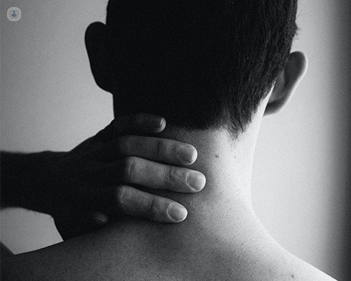 The back of a man's neck. He is pressing his hand on it to alleviate pain.