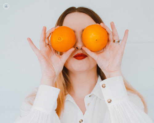 Woman placing oranges, which are good for your eye health, to her eyes