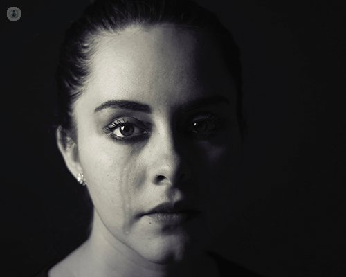 A black and white image of a woman who has been crying. She looks into the camera with a sad expression.