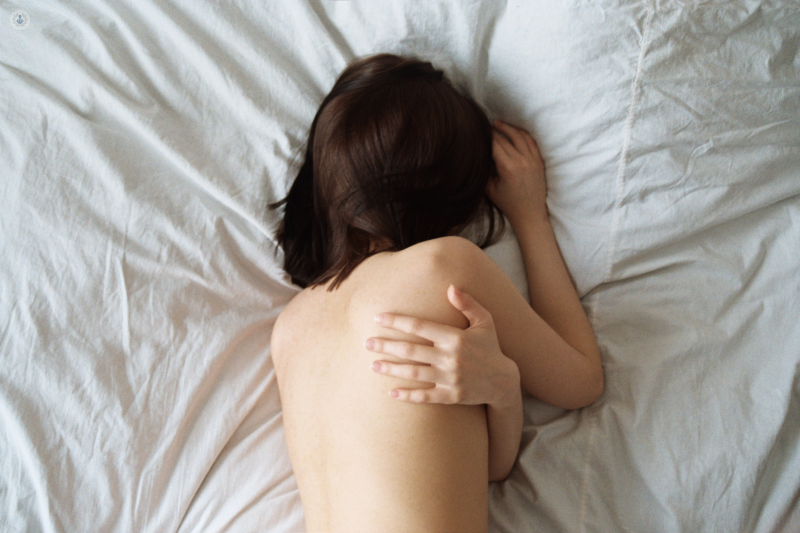 Woman in bed holding her shoulder