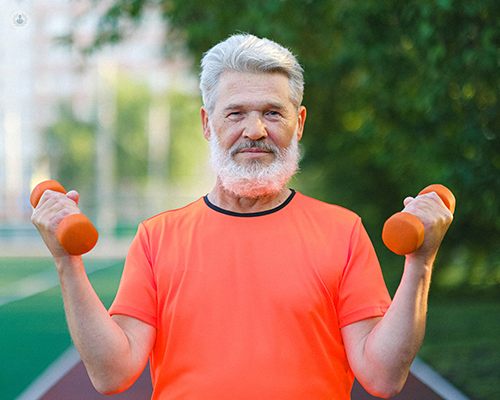 A man in his athletic clothing holding two small dumbbells while looking into the camera