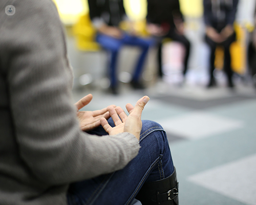 The focus is on the hands of a person who is talking to a group of people who are all sat on chairs in a circle, perhaps in a dialectical behavior therapy session. This is beneficial for many with borderline personality disorder.