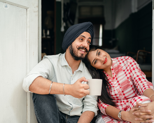 Happy Sikh couple sat in the doorway of a house, with the ladies' head leaning on her partner's shoulder