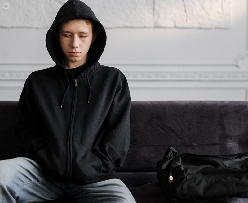 Boy with chronic pain at a psychology appointment, wearing a black hoodie and with a sad expression