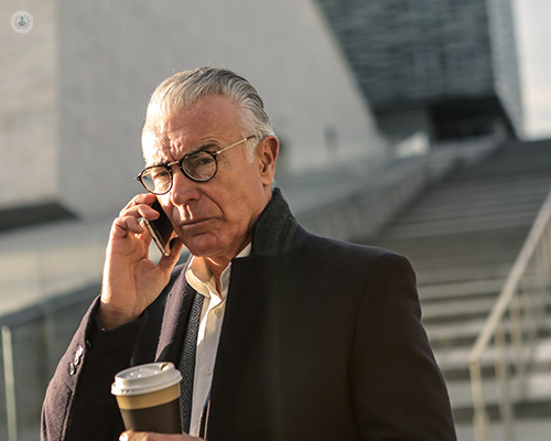 An older man is on his mobile phone having a phone call, dressed in business attire.