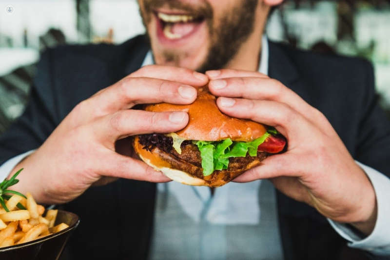 Man eating a burger, which can lead to a fatty liver disease