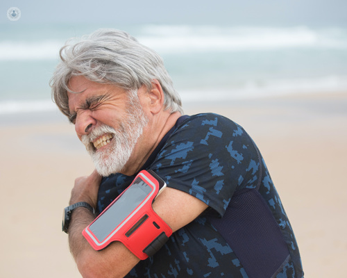 Man with shoulder pain on the beach, grimacing