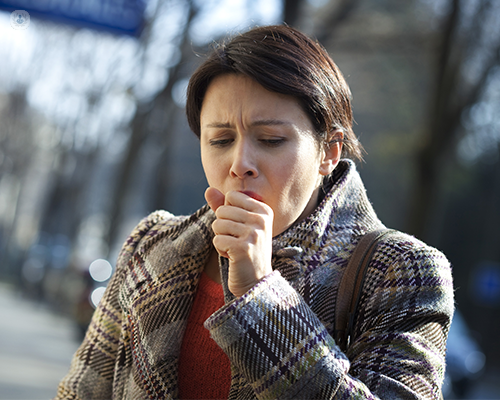 A woman is coughing into her hand, which is not a safe way to cough -coughing into the crease of an elbow or into a tissue is better at preventing the spread of a virus- and consequently she may pass her infection to others.