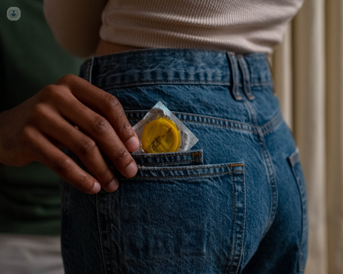 Couple, with a man pulling a condom, which helps to prevent genital warts, out a woman's back pocket