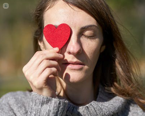 Young woman in the sunshine holding red paper heart cut out to her eye